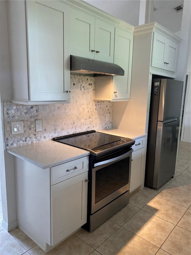 kitchen featuring light stone countertops, light tile flooring, appliances with stainless steel finishes, wall chimney range hood, and tasteful backsplash