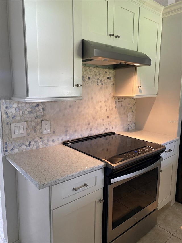 kitchen featuring light tile floors, wall chimney range hood, light stone countertops, stainless steel electric range oven, and white cabinetry