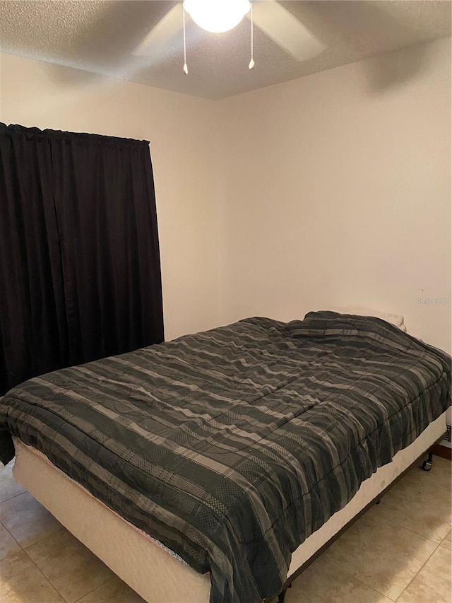 bedroom featuring a textured ceiling, ceiling fan, and light tile floors