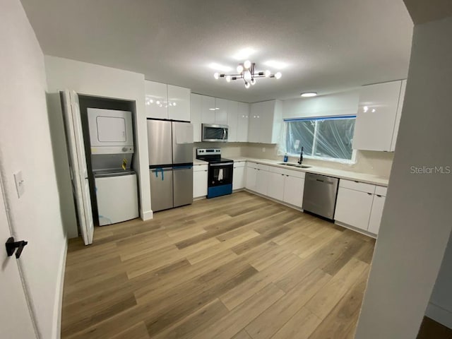 kitchen with stacked washer and clothes dryer, stainless steel appliances, sink, white cabinetry, and light hardwood / wood-style floors