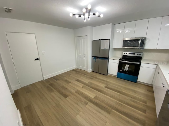 kitchen with an inviting chandelier, white cabinetry, stainless steel appliances, and light wood-type flooring