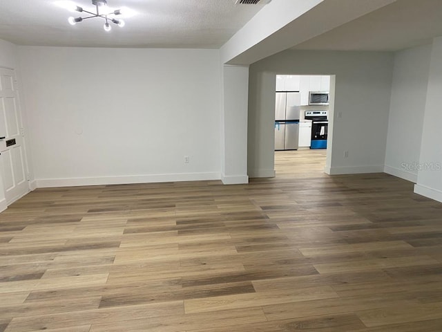 spare room featuring an inviting chandelier, a textured ceiling, and light wood-type flooring