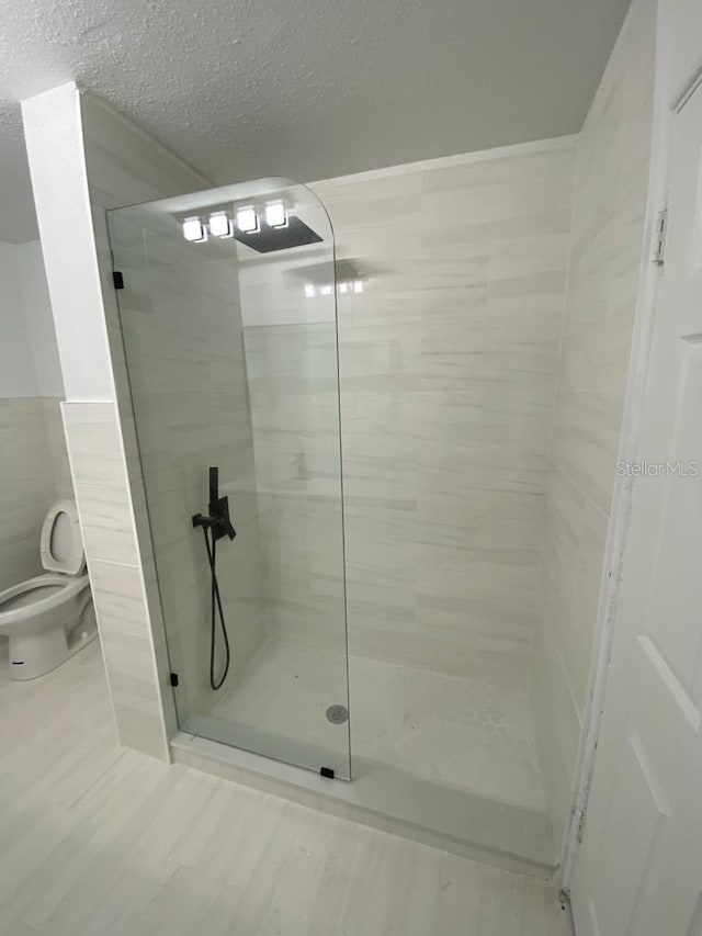 bathroom with toilet, a textured ceiling, a tile shower, and tile walls