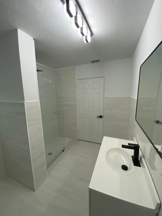 bathroom with vanity, tiled shower, a textured ceiling, and tile walls