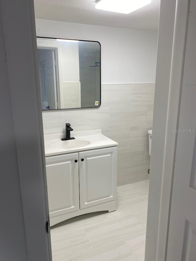 bathroom featuring vanity, toilet, and tile walls