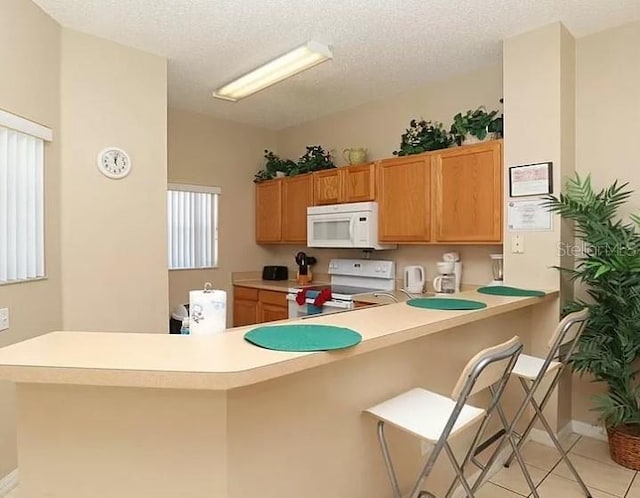 kitchen featuring a breakfast bar area, light countertops, light tile patterned flooring, white appliances, and a peninsula