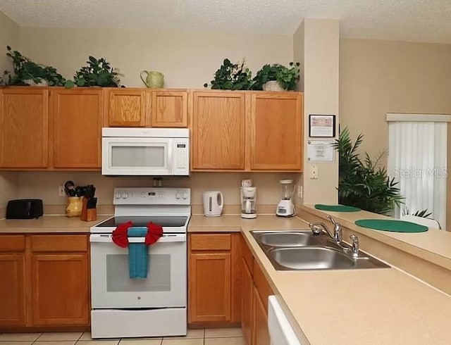 kitchen featuring light tile patterned floors, light countertops, a sink, a textured ceiling, and white appliances