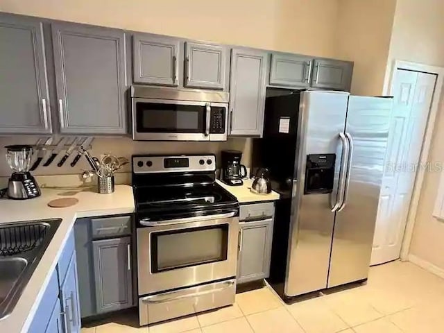 kitchen with light tile floors, appliances with stainless steel finishes, gray cabinets, and sink