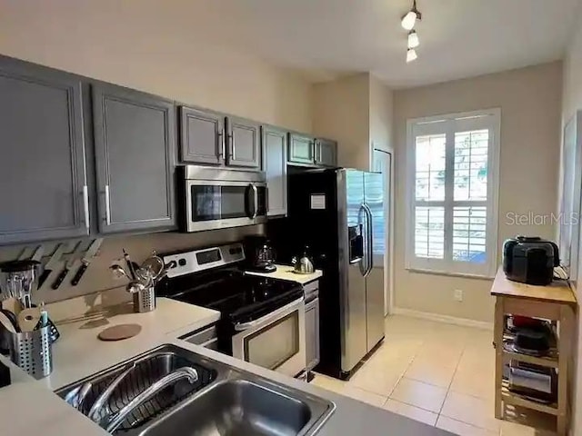 kitchen with sink, light tile floors, gray cabinetry, rail lighting, and stainless steel appliances