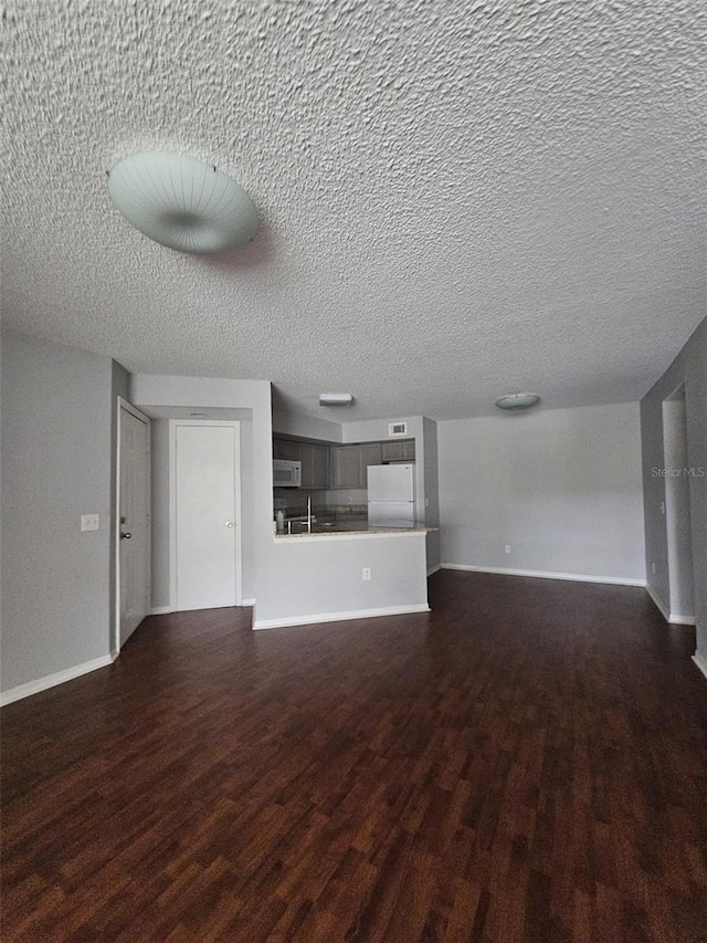 unfurnished living room featuring dark wood-type flooring, sink, and a textured ceiling