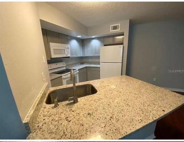 kitchen featuring light stone counters, sink, white appliances, and a textured ceiling