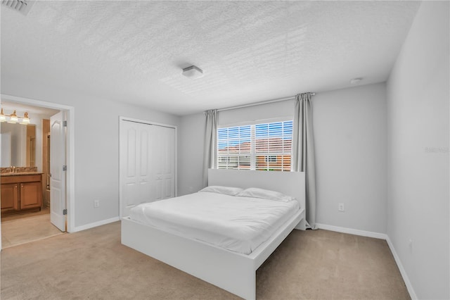 carpeted bedroom with sink, a textured ceiling, a closet, and ensuite bathroom