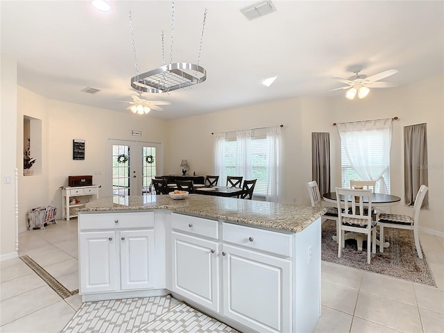 kitchen with light tile floors, light stone countertops, ceiling fan, french doors, and white cabinetry