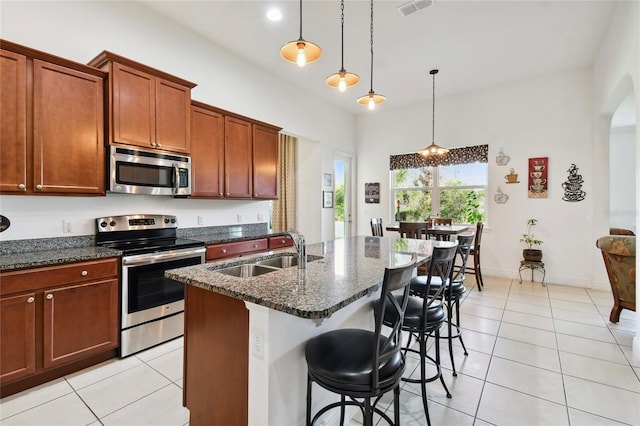 kitchen with light tile floors, decorative light fixtures, dark stone counters, appliances with stainless steel finishes, and sink