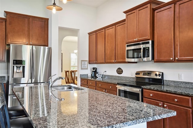 kitchen featuring appliances with stainless steel finishes, dark stone counters, sink, and a center island with sink