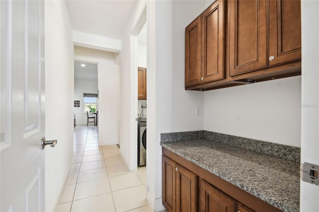 kitchen with light tile floors, dark stone countertops, and washer / clothes dryer