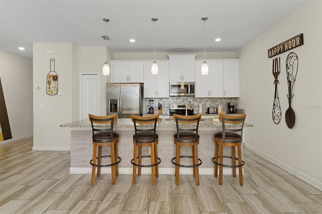 kitchen with backsplash, white cabinetry, a breakfast bar area, a center island with sink, and stainless steel appliances