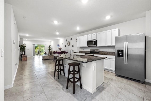 kitchen with stainless steel appliances, dark stone counters, white cabinets, a breakfast bar, and a kitchen island with sink