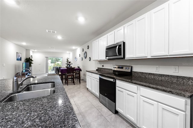 kitchen with light tile patterned floors, appliances with stainless steel finishes, white cabinetry, dark stone countertops, and sink