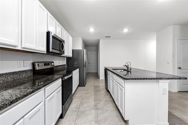 kitchen featuring dark stone counters, a center island with sink, sink, white cabinetry, and appliances with stainless steel finishes