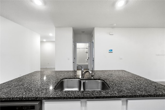 kitchen with sink, white cabinets, a textured ceiling, and dark stone countertops