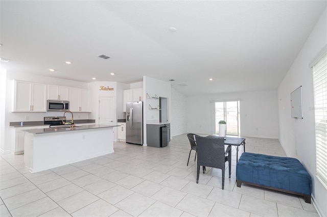 kitchen featuring an island with sink, sink, light tile floors, appliances with stainless steel finishes, and white cabinetry