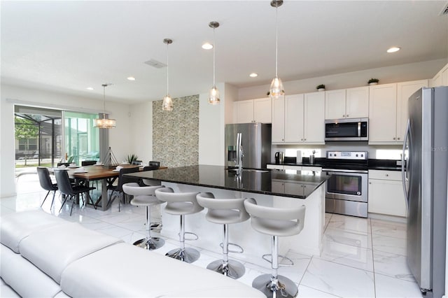 kitchen featuring a kitchen breakfast bar, hanging light fixtures, a center island with sink, stainless steel appliances, and light tile flooring