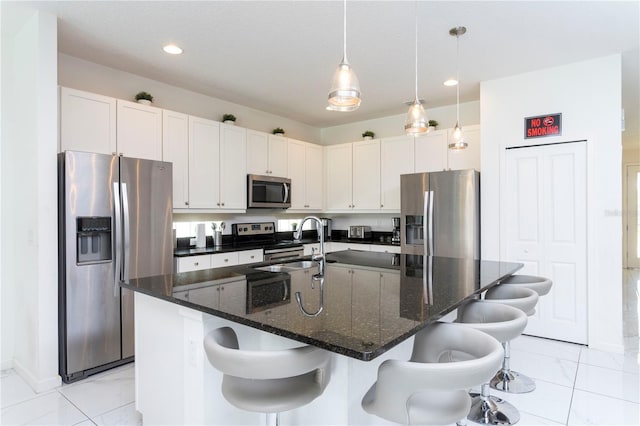 kitchen with pendant lighting, a kitchen breakfast bar, a center island with sink, appliances with stainless steel finishes, and dark stone countertops