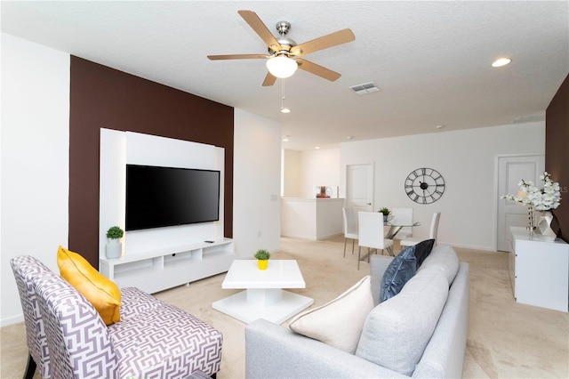 living room featuring a textured ceiling, ceiling fan, and light colored carpet