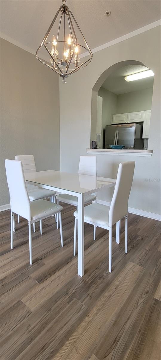 dining space with dark wood-type flooring, crown molding, and an inviting chandelier