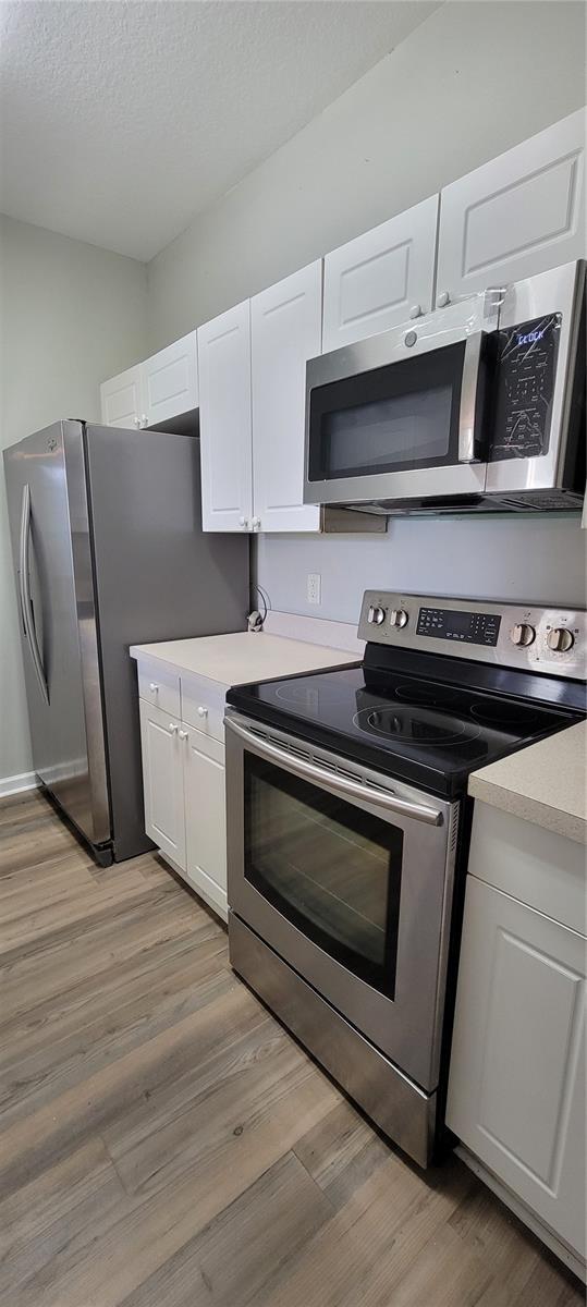 kitchen with appliances with stainless steel finishes, white cabinets, a textured ceiling, and light hardwood / wood-style floors