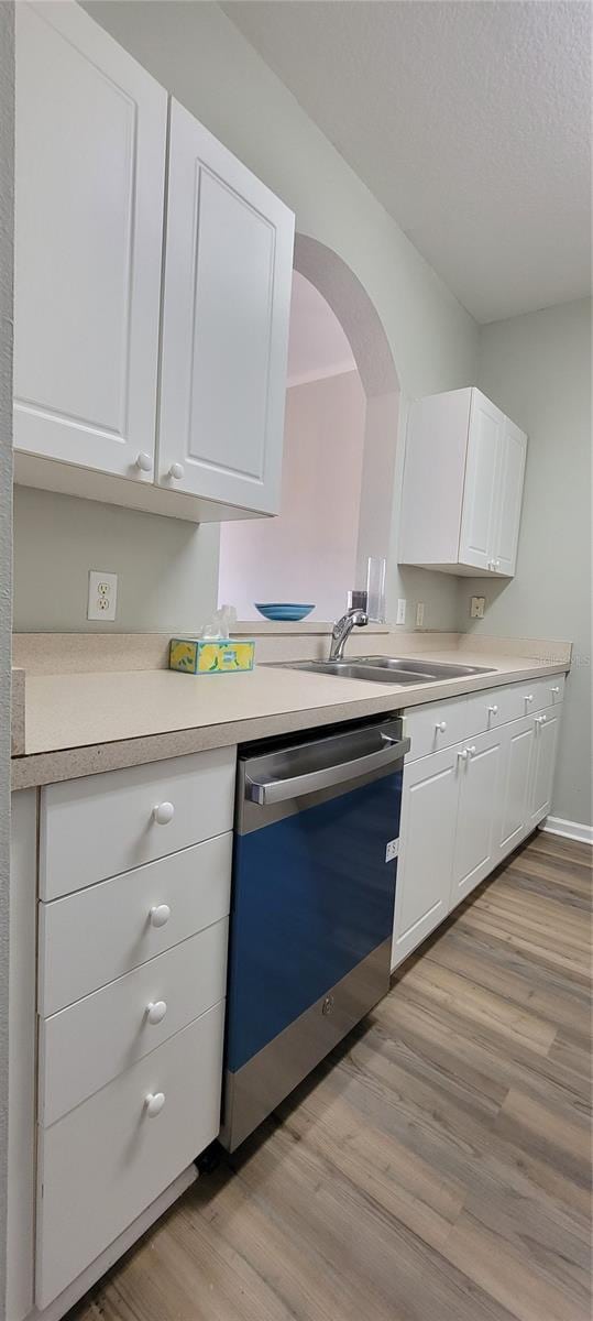 kitchen with white cabinetry, sink, stainless steel dishwasher, light hardwood / wood-style floors, and a textured ceiling