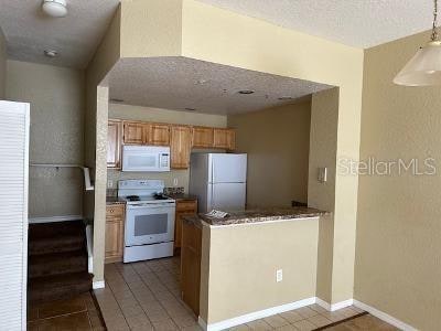 kitchen with a textured ceiling, white appliances, and light tile flooring