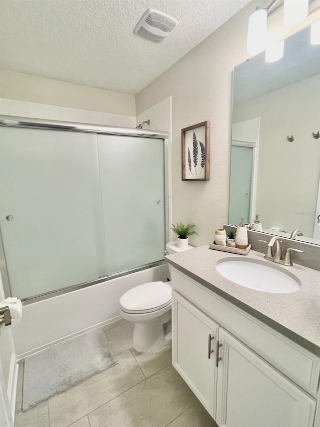 full bathroom with toilet, vanity with extensive cabinet space, combined bath / shower with glass door, tile flooring, and a textured ceiling