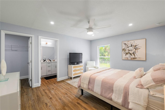 bedroom with a spacious closet, a closet, hardwood / wood-style flooring, ensuite bath, and ceiling fan