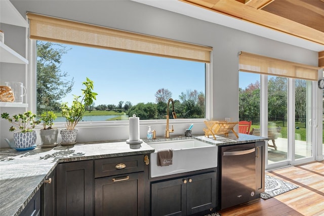 kitchen with dishwasher, sink, light stone counters, light hardwood / wood-style floors, and a water view