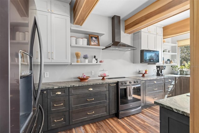 kitchen with white cabinetry, appliances with stainless steel finishes, wall chimney range hood, and dark stone counters