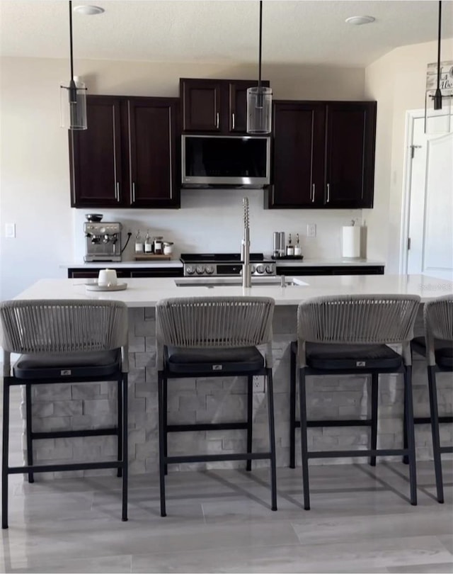 kitchen with an island with sink, dark brown cabinets, pendant lighting, and a breakfast bar