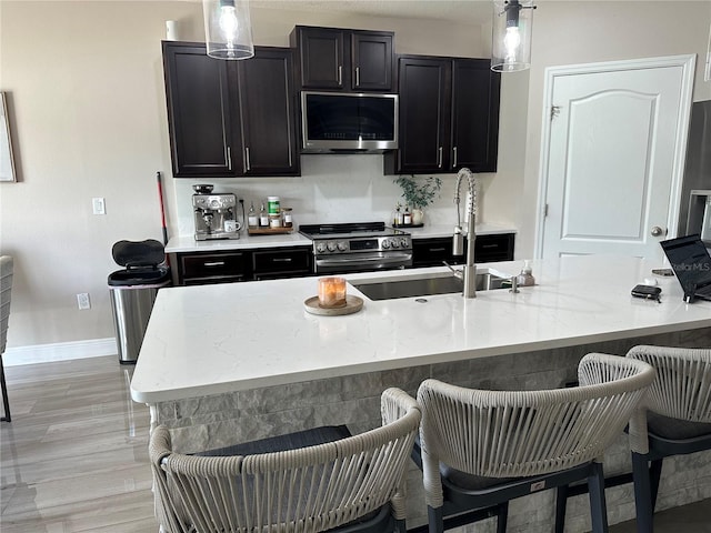 kitchen with sink, a kitchen breakfast bar, light hardwood / wood-style floors, decorative light fixtures, and high end stainless steel range oven