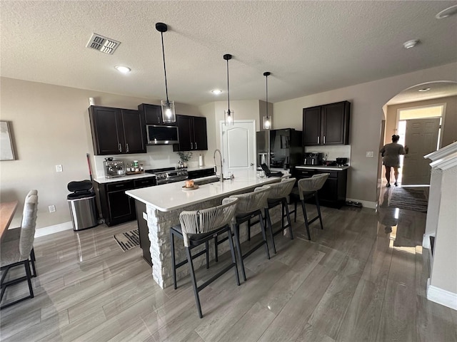 kitchen with decorative light fixtures, appliances with stainless steel finishes, a breakfast bar, light hardwood / wood-style flooring, and an island with sink