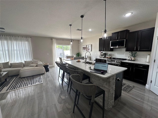 kitchen featuring a kitchen island with sink, sink, hanging light fixtures, appliances with stainless steel finishes, and a textured ceiling