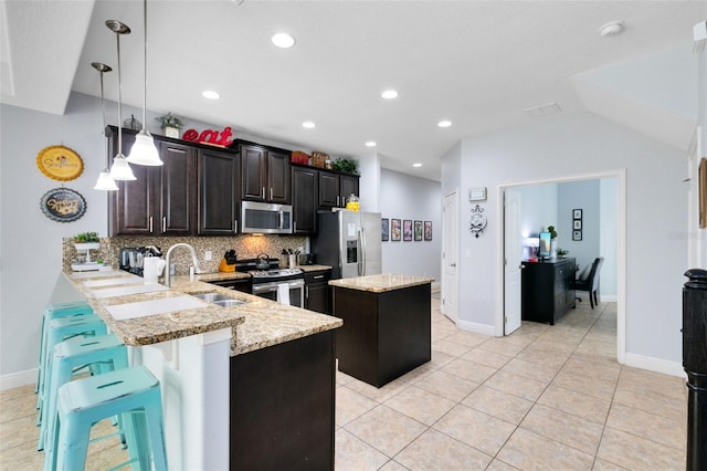 kitchen featuring kitchen peninsula, stainless steel appliances, sink, a center island, and a breakfast bar area