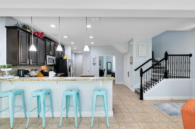 kitchen with a breakfast bar area, decorative backsplash, light stone counters, and appliances with stainless steel finishes