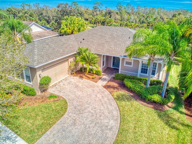 ranch-style home with a shingled roof, decorative driveway, a front lawn, and stucco siding