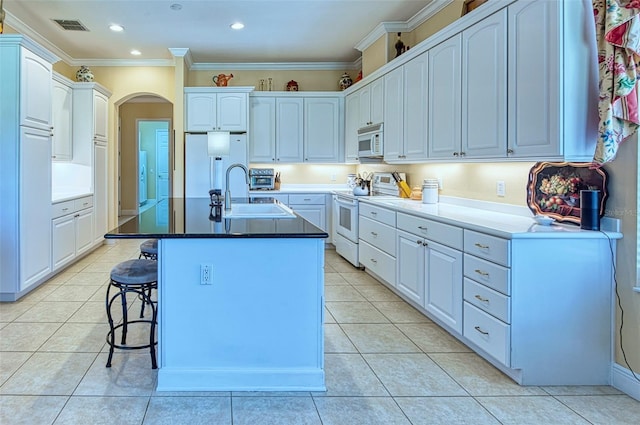 kitchen featuring white cabinetry, light tile flooring, white appliances, sink, and an island with sink