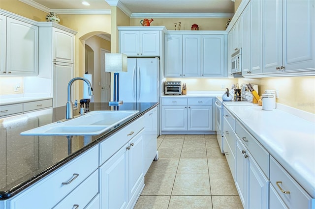 kitchen with dark stone counters, white cabinetry, light tile floors, white appliances, and sink