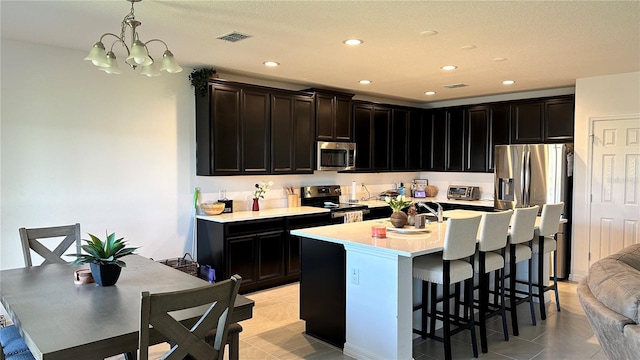 kitchen featuring a kitchen island with sink, an inviting chandelier, stainless steel appliances, a breakfast bar area, and pendant lighting