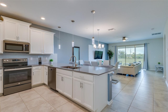 kitchen with stainless steel appliances, light tile floors, decorative light fixtures, white cabinetry, and sink