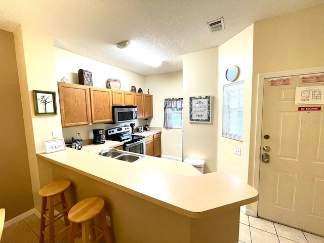 kitchen with a kitchen bar, kitchen peninsula, light tile patterned floors, and stainless steel appliances