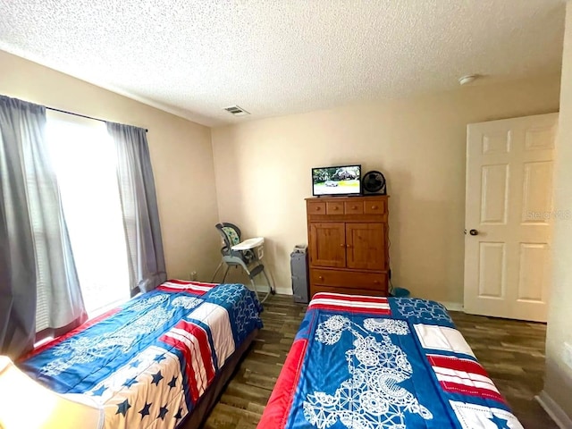 bedroom featuring multiple windows, dark wood-type flooring, and a textured ceiling